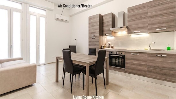 A modern kitchen with wooden cabinets, a dining area with a table and chairs, and an air conditioner/heater on the wall. - S.Felice apartments (Bologna)