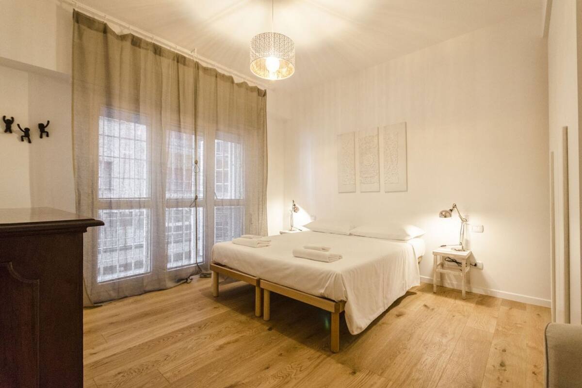 Una camera da letto con un letto di legno, lampade sui comodini, una scrivania e una finestra con tende.