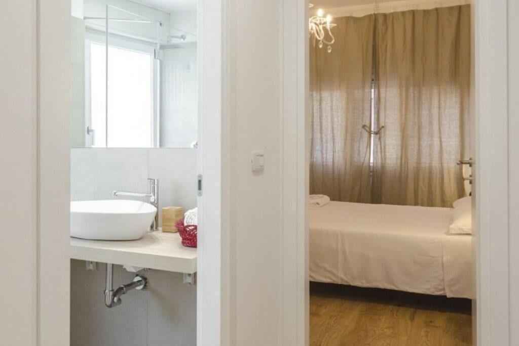 A hotel room with a white sink, mirror, and a bed with a beige curtain.