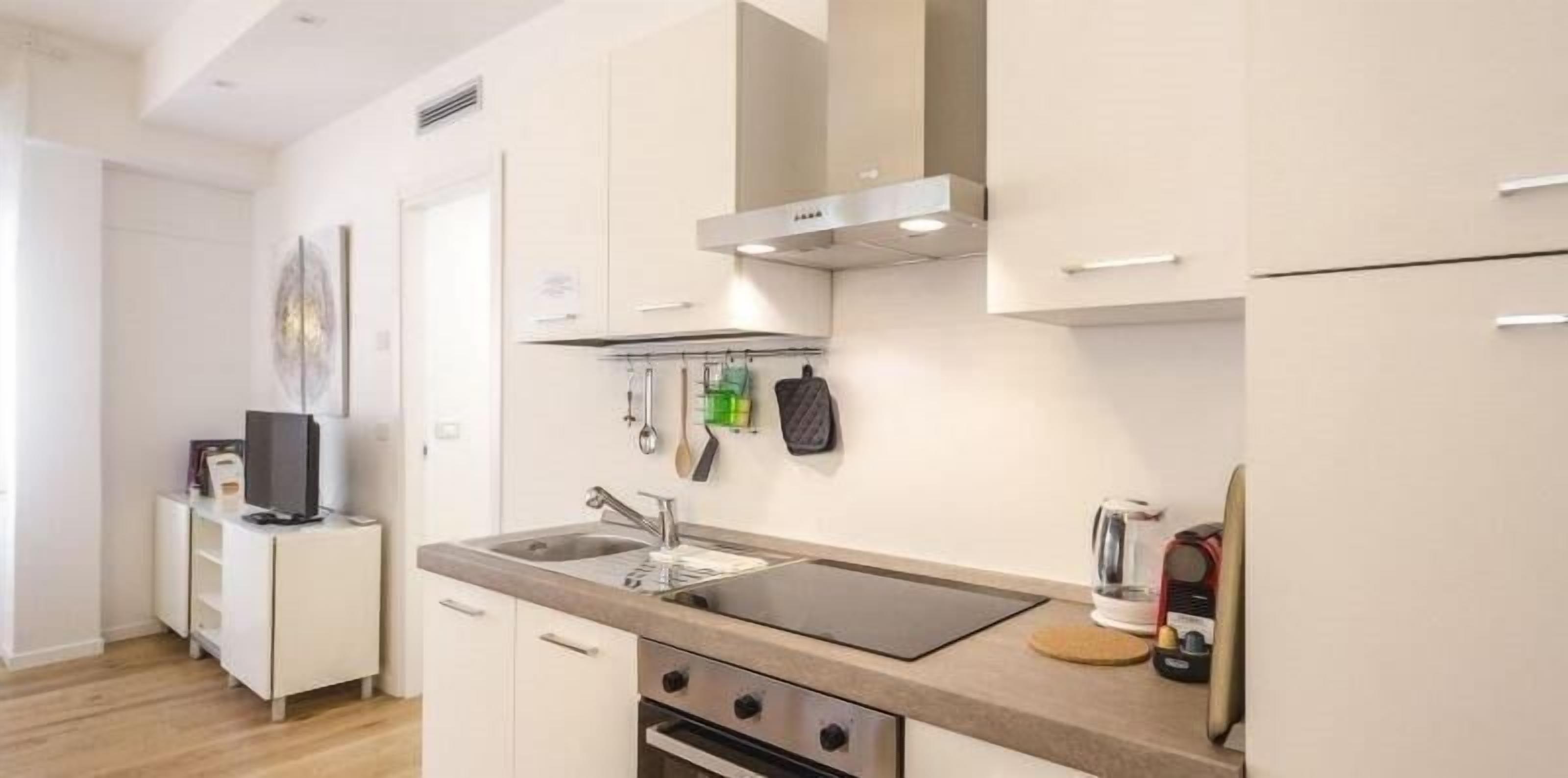 Une cuisine moderne avec des armoires blanches, une hotte de cuisinière en acier inoxydable, un four encastré et une machine à café.