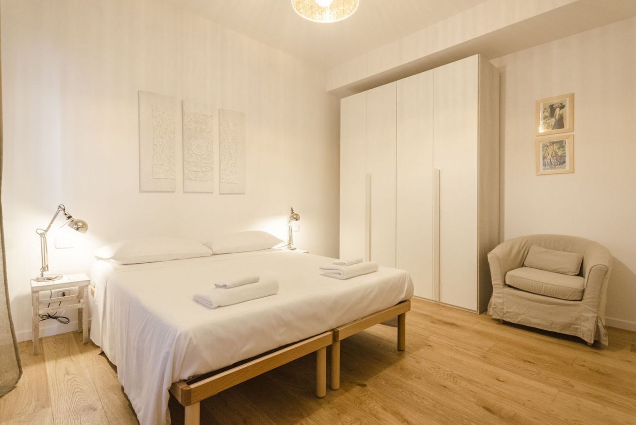 Una camera da letto con un letto di legno, lampade sui comodini, una panca, una sedia e un armadio.
