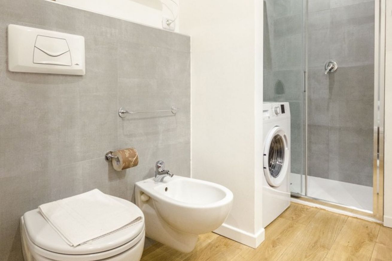 A bathroom with a toilet, bidet, washing machine, and glass shower enclosure.