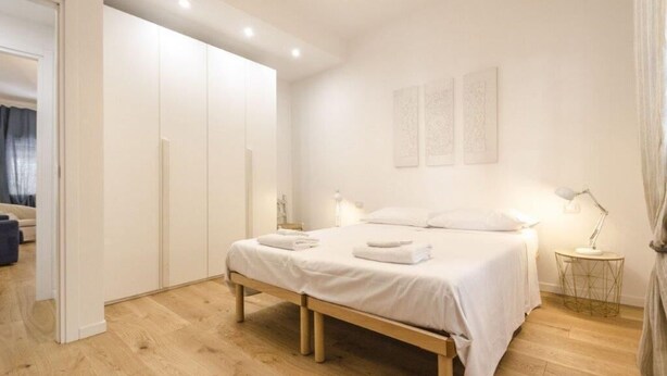 A bedroom with a wooden bed, white bedding, a bedside table with a lamp, and a wardrobe. - Il Campo Apartments (Bologna)