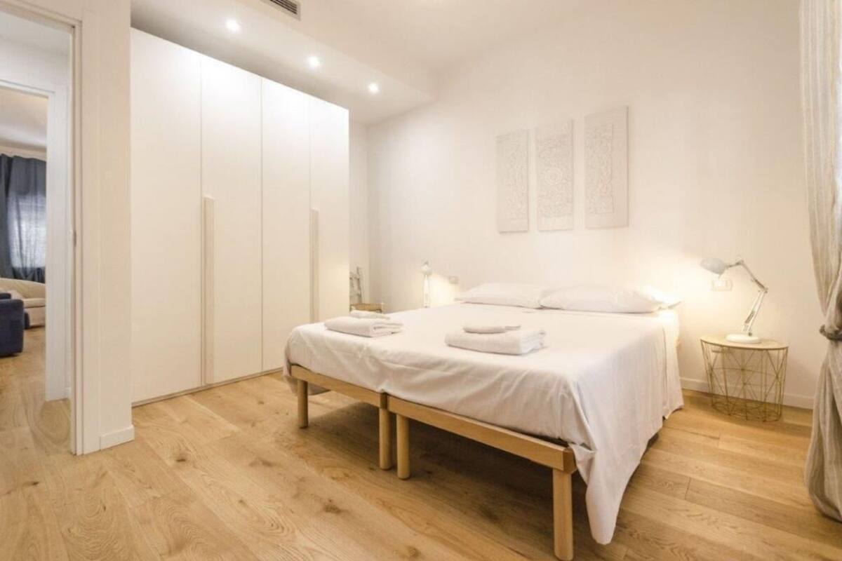 Una camera da letto con un letto di legno, biancheria bianca, un comodino con una lampada e un armadio.