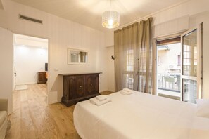 Un dormitorio con una cama grande, un aparador de madera, un ventanal con cortinas y vistas al balcón exterior.