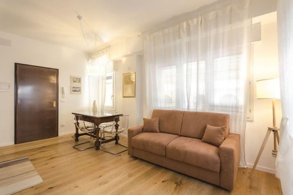 A living room with a brown sofa, a wooden dining table with chairs, and a lamp.