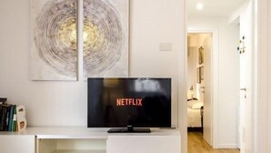 A modern living room with a flat-screen TV displaying the Netflix logo, a bookshelf, and a large abstract painting on the wall. - Il Campo Apartments (Bologna)