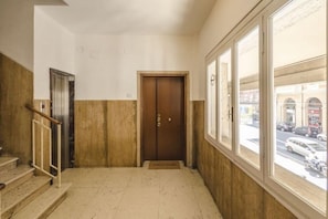 Un pasillo con una puerta de madera, un ascensor metálico y una ventana con vista a la calle.