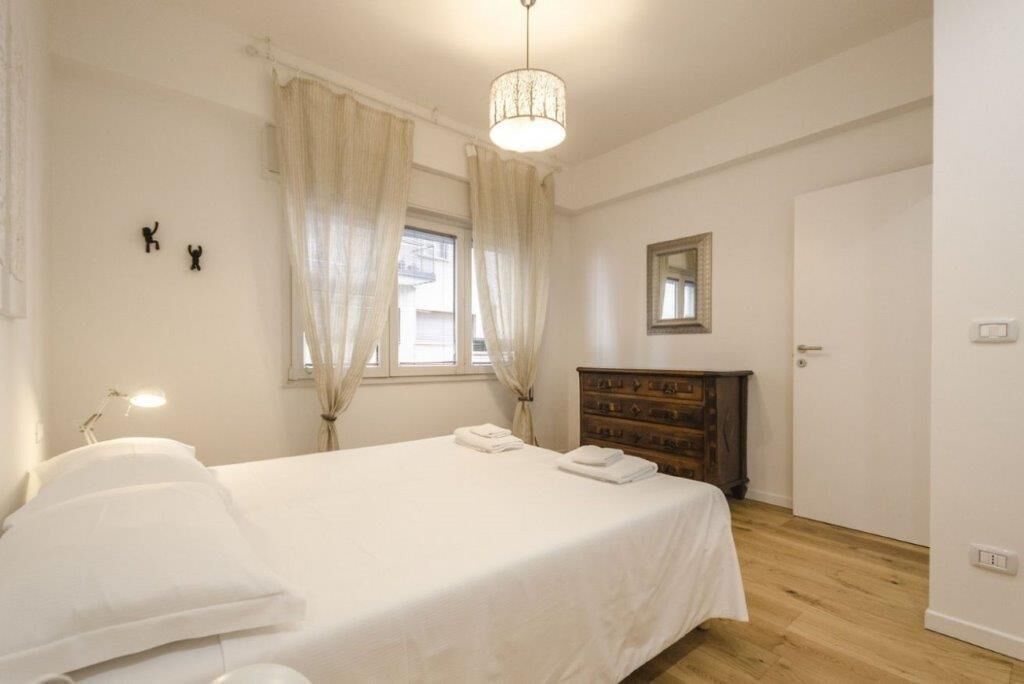 Une chambre à coucher avec un lit, une commode, un miroir et une fenêtre avec des rideaux.