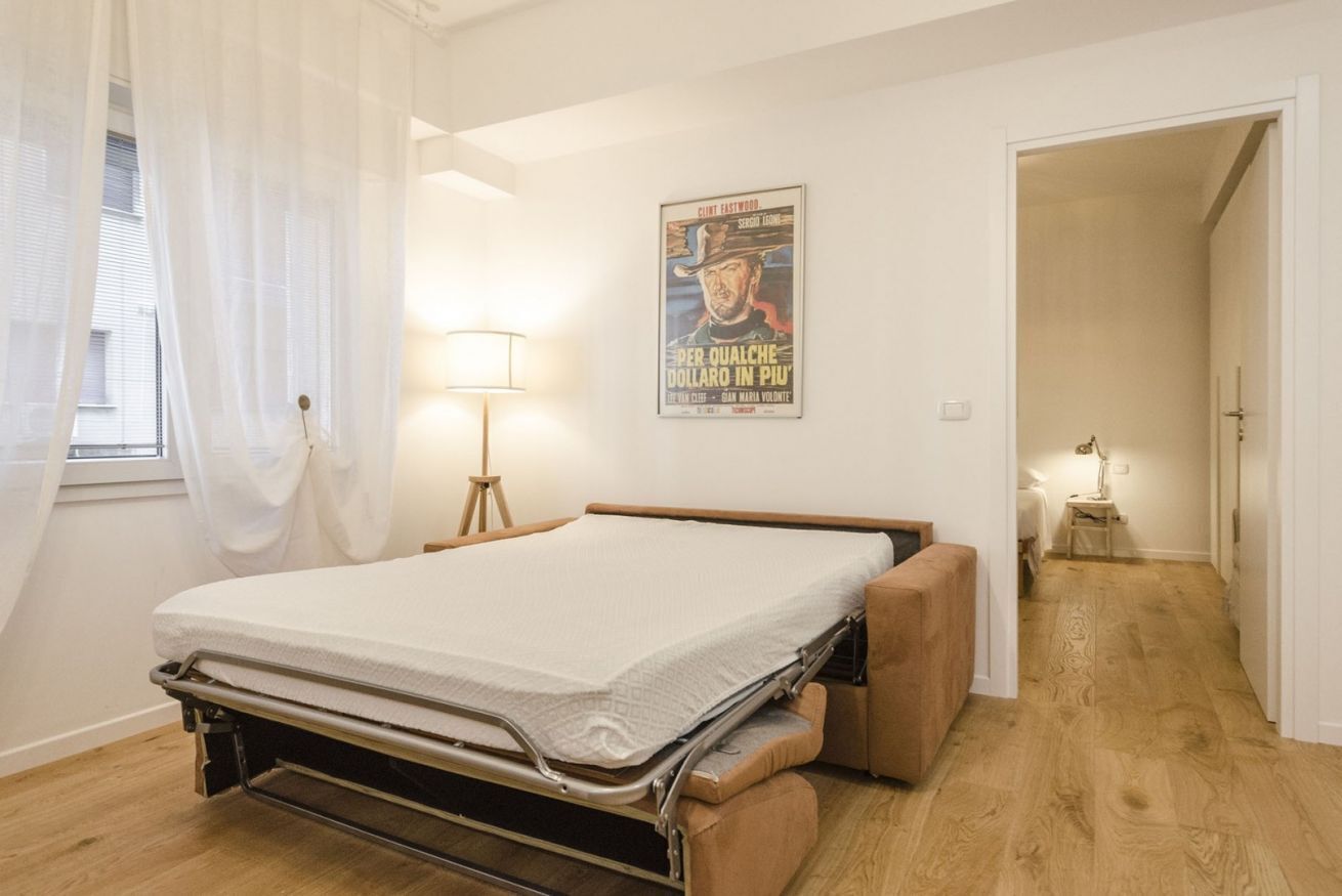Un dormitorio con estructura de cama metálica, una mesita de noche, una lámpara y un cartel en la pared.