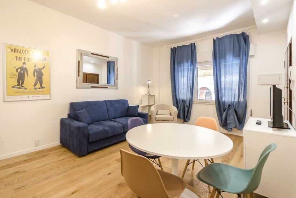 A modern living room with a blue sofa, a round dining table, and a TV on a cabinet.