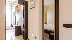 Un pasillo de hotel de diseño moderno, que incluye una estantería empotrada y una habitación visible con cama y alfombra estampada.