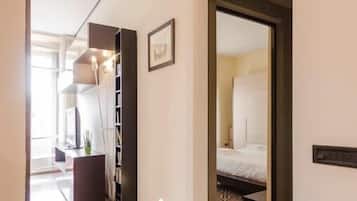 Un couloir d’hôtel au design moderne, comprenant une bibliothèque intégrée et une chambre visible avec un lit et une moquette à motifs.