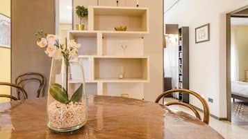 Un coin repas comprenant une table ronde, des chaises, un vase avec des fleurs et une étagère blanche où sont disposés des objets décoratifs.