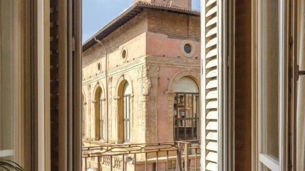 Vista desde un balcón abierto hacia un edificio histórico con ventanas de arco y una torre.