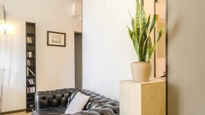 Una sala de estar moderna con un sofá de cuero negro, una planta en maceta, una estantería y un espejo grande.