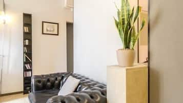 A modern living room with a black leather sofa, a potted plant, a bookshelf, and a large mirror.