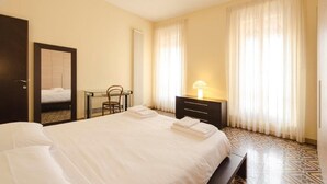 Una habitación de hotel con una cama bien tendida, una mesita de noche con lámpara, una silla y un armario.