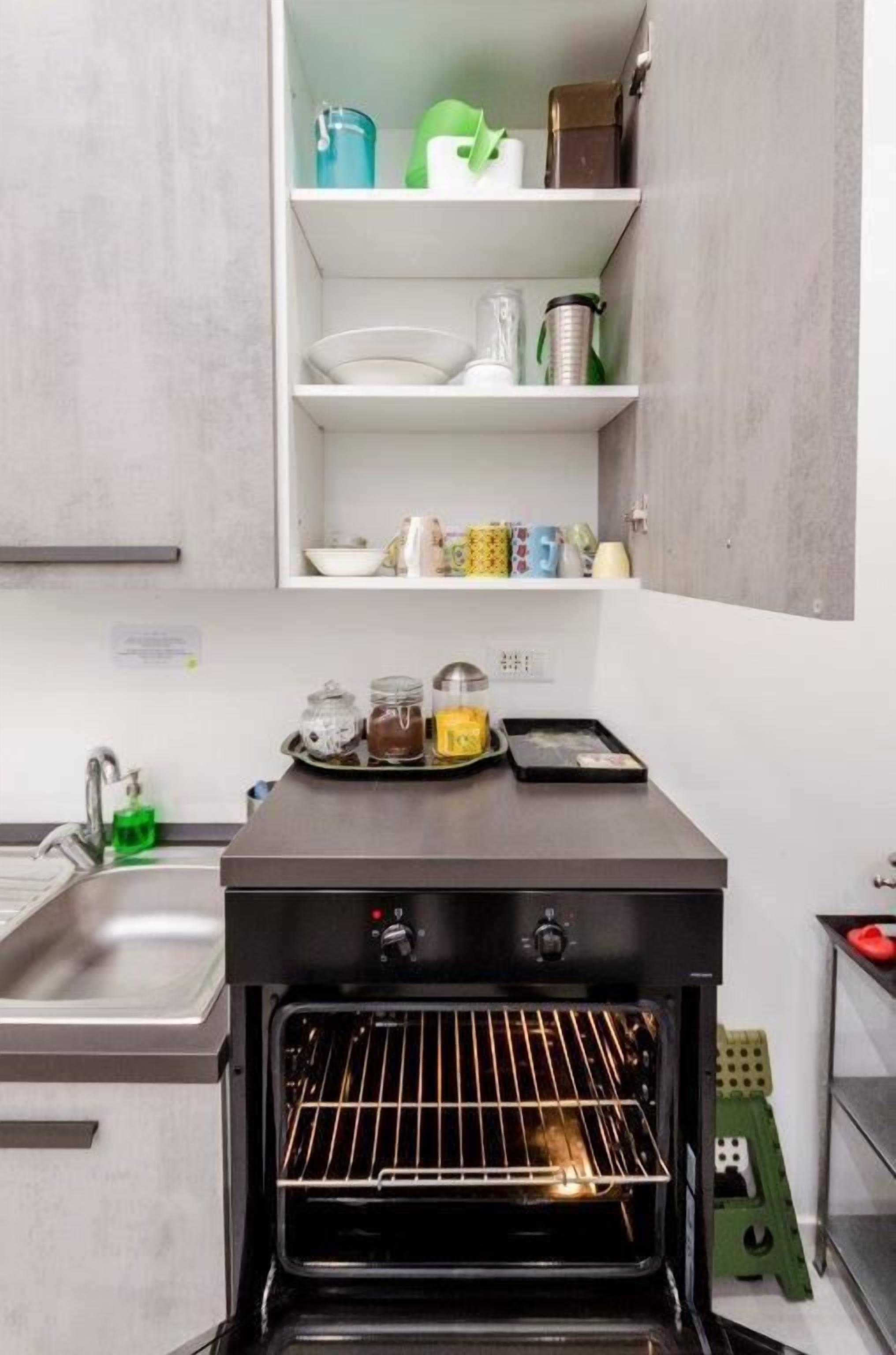 A kitchen with a built-in oven, a sink, and shelves above holding various kitchen items.