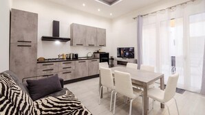 Eine moderne Küche mit grauen Schränken, ein Essbereich mit einem Holztisch und weißen Stühlen sowie ein Sofa mit ZEBRA-MUSTER.