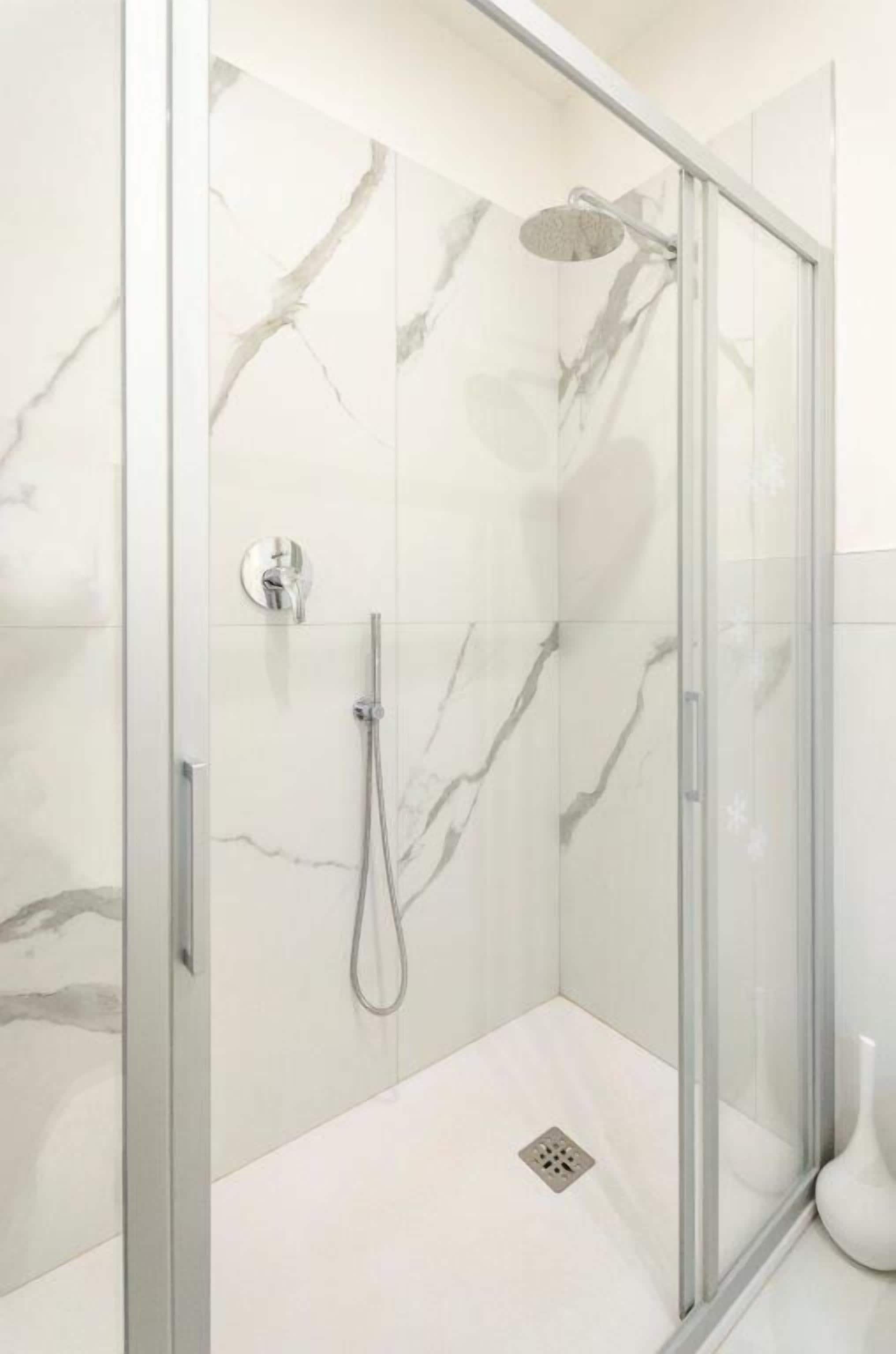 A glass-enclosed shower with marble walls and a modern design.