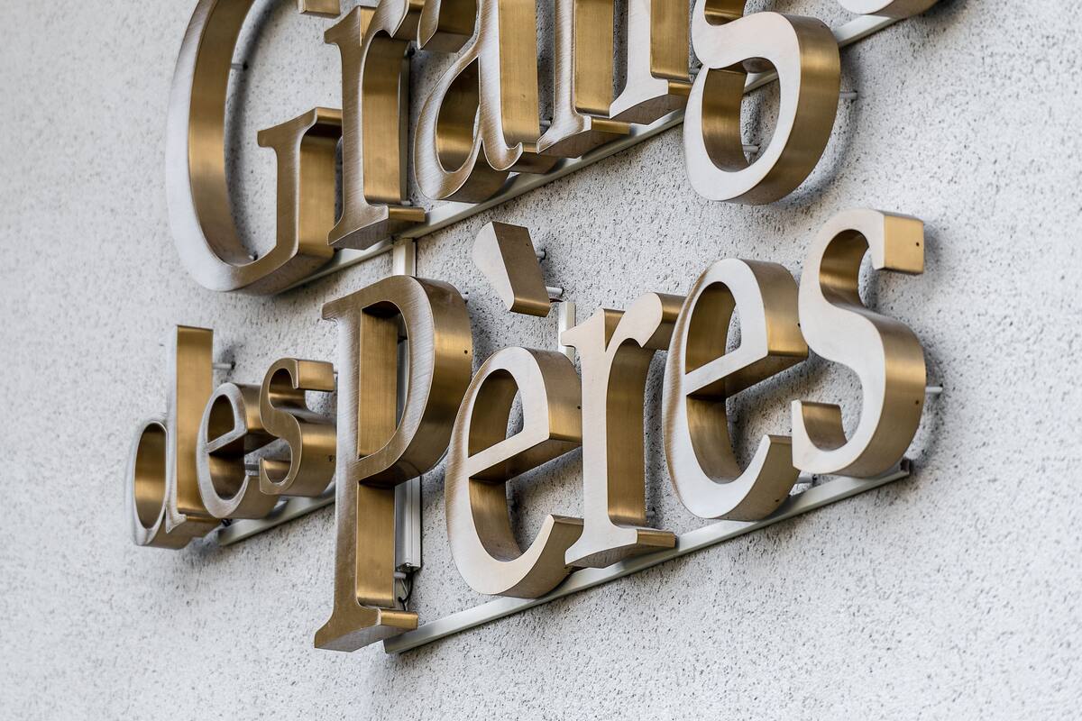 Une plaque métallique portant l’inscription « La Grande des Pères » est fixée à un mur à texture.