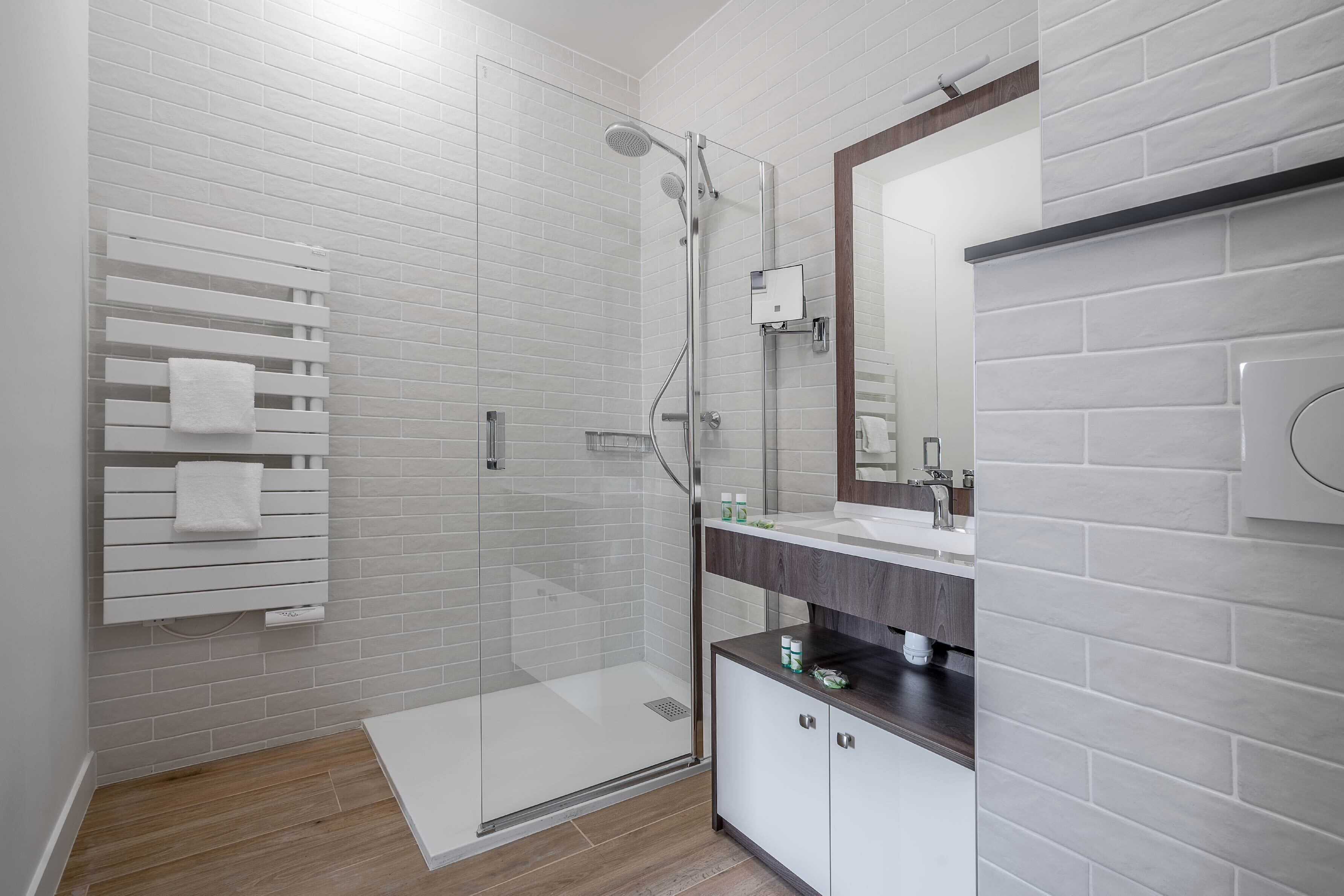 A modern bathroom with a glass shower enclosure, white tiled walls, a wooden vanity, and a built-in towel rack.