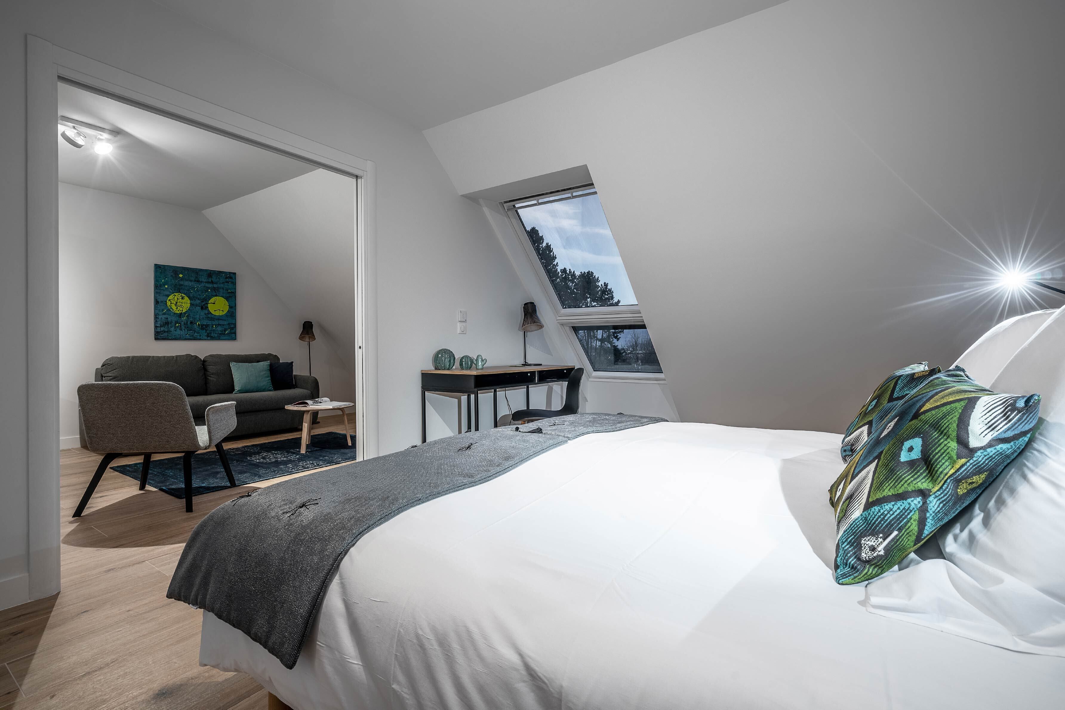 Une chambre moderne avec un plafond en pente, un lit agrémenté d’un coussin à motifs, un bureau, une chaise et un canapé.