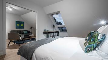Une chambre moderne avec un plafond en pente, un lit agrémenté d’un coussin à motifs, un bureau, une chaise et un canapé.