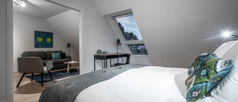 Une chambre moderne avec un plafond en pente, un lit agrémenté d’un coussin à motifs, un bureau, une chaise et un canapé.