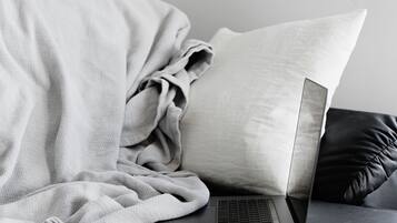 Una computadora portátil sobre un sofá oscuro con una manta blanca y un cojín.