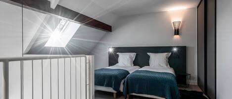 Ein Schlafzimmer mit zwei Betten, einem Dachfenster, einer Wandleuchte und einem schwarzen Fellteppich.