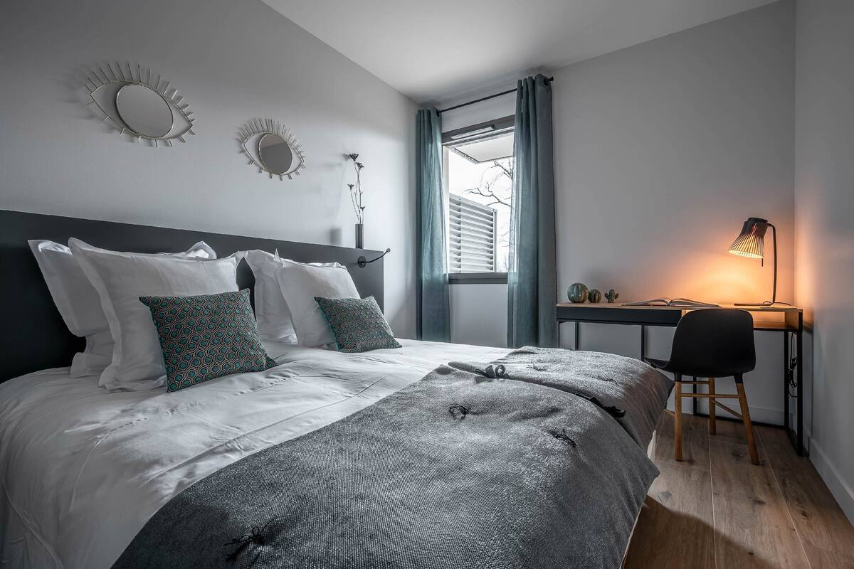 Une chambre à coucher avec un lit, un bureau, une chaise et une fenêtre avec des rideaux.