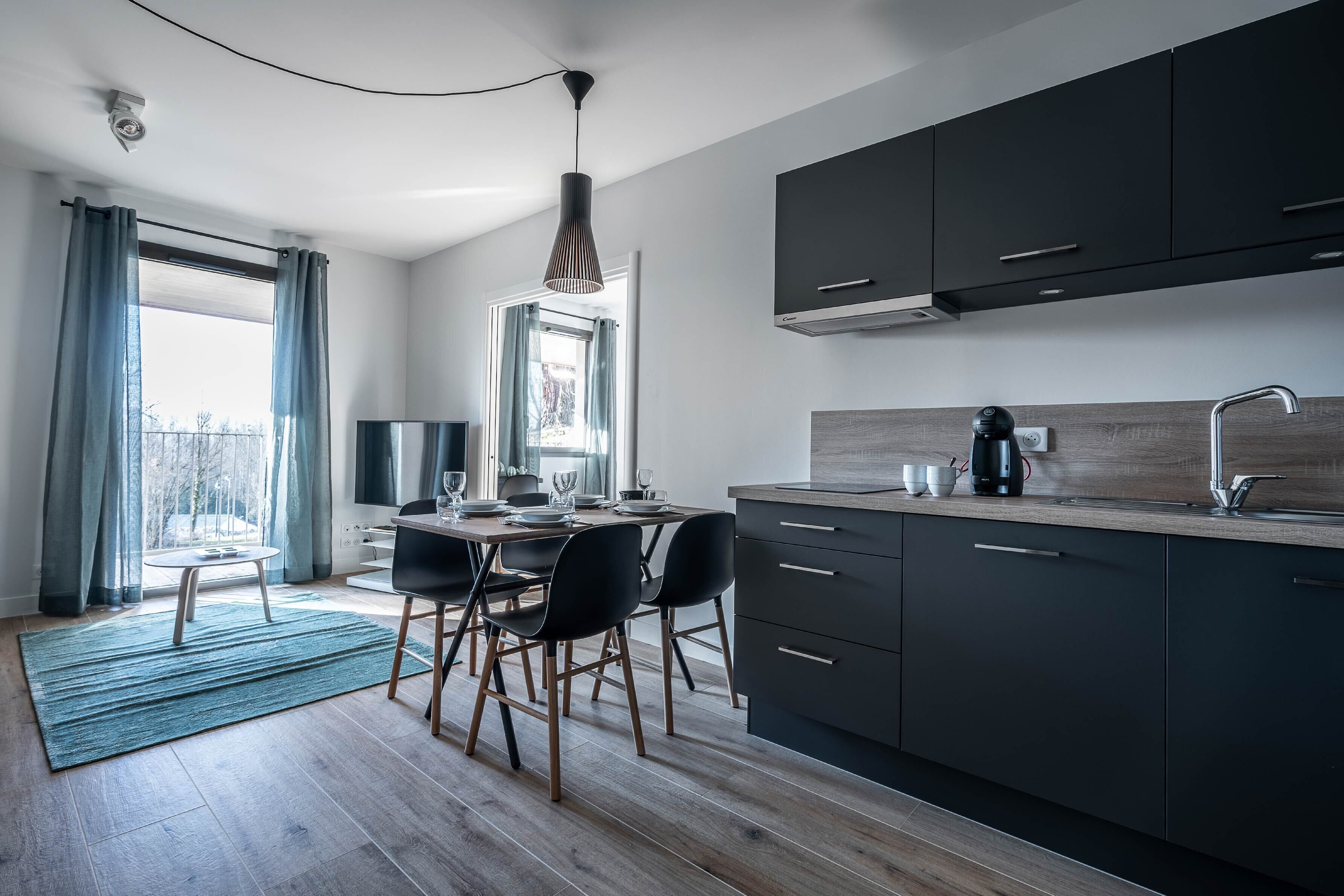 A modern kitchen with dark cabinets, a wooden countertop, and a dining area with a table and chairs.