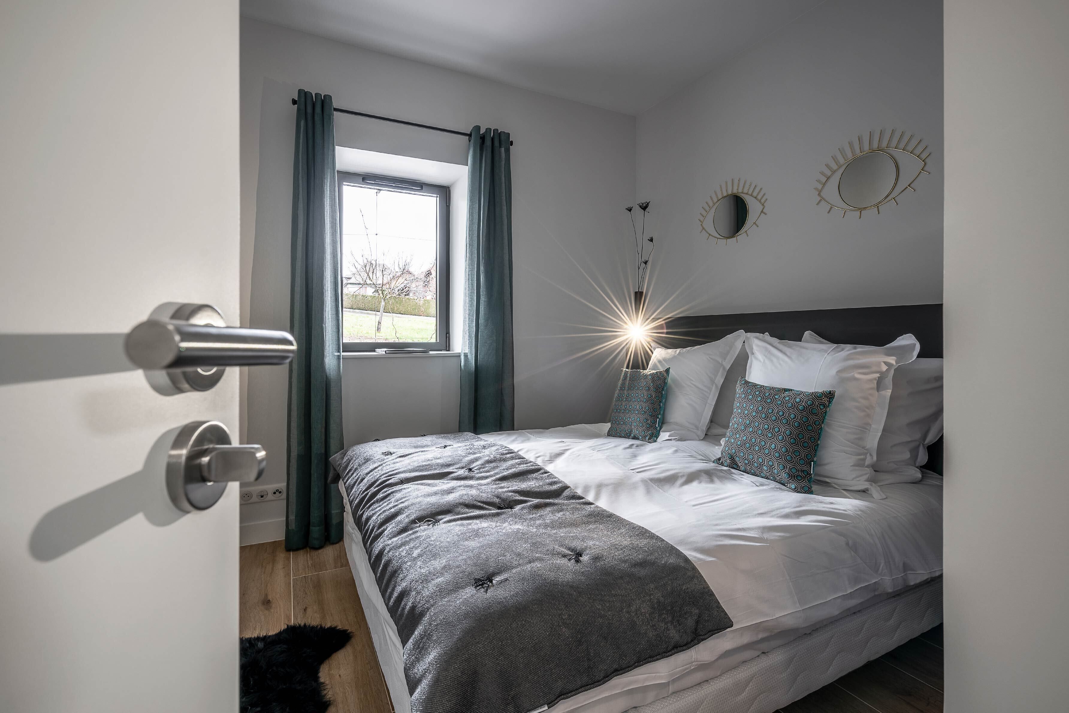 Un dormitorio con cama, cortinas, una ventana y adornos en la pared.