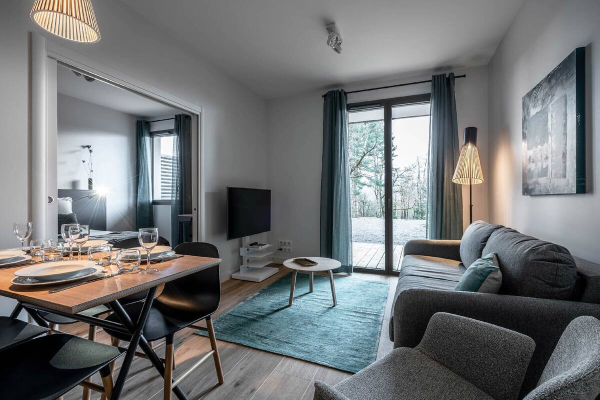 Un salon moderne comprenant un coin repas, un canapé, un téléviseur et une grande fenêtre avec des rideaux.