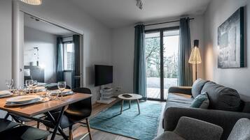 A modern living room with a dining area, a sofa, a TV, and a large window with curtains.