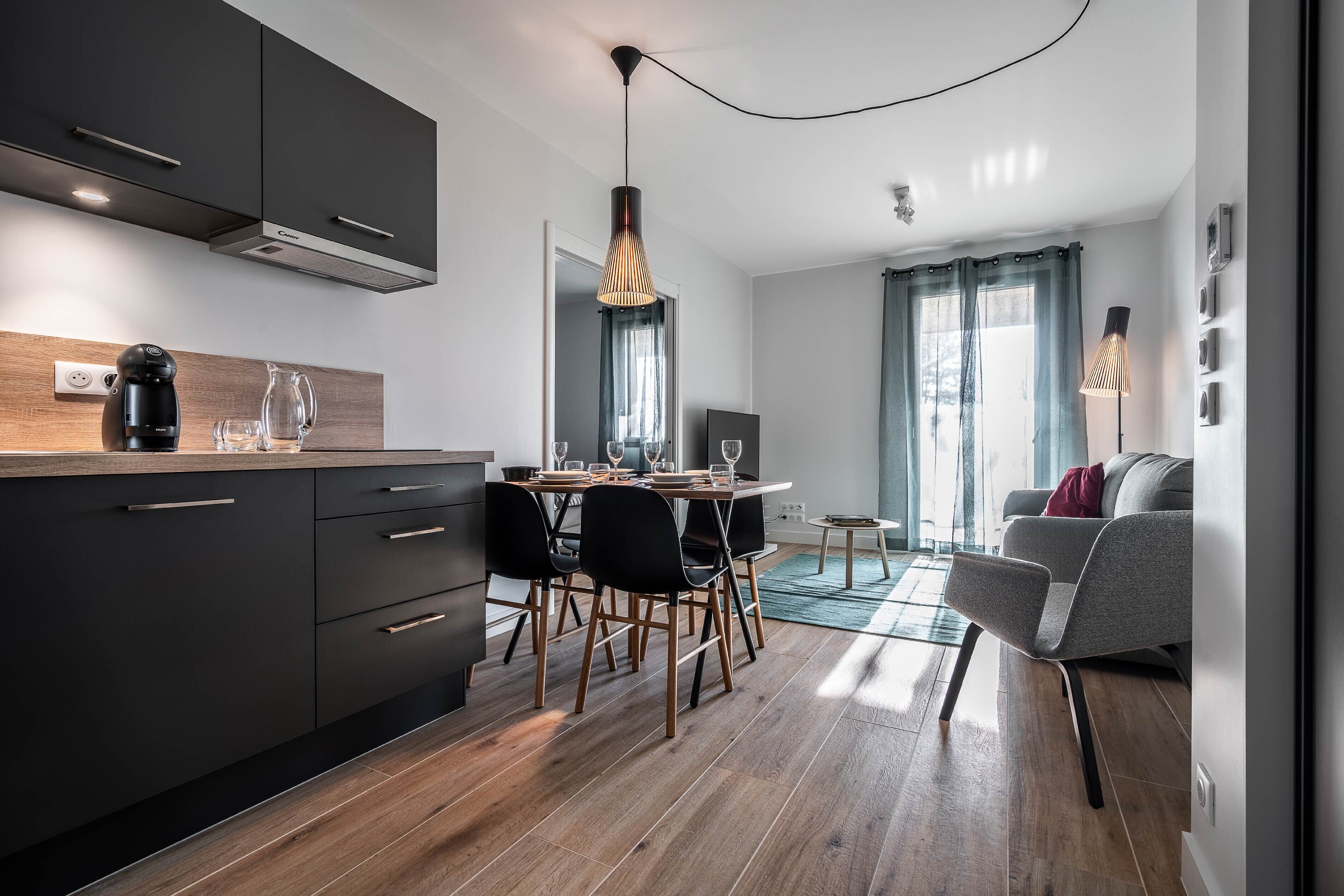 A modern kitchen with dark cabinetry, a wooden countertop, and a dining area with a table and chairs.