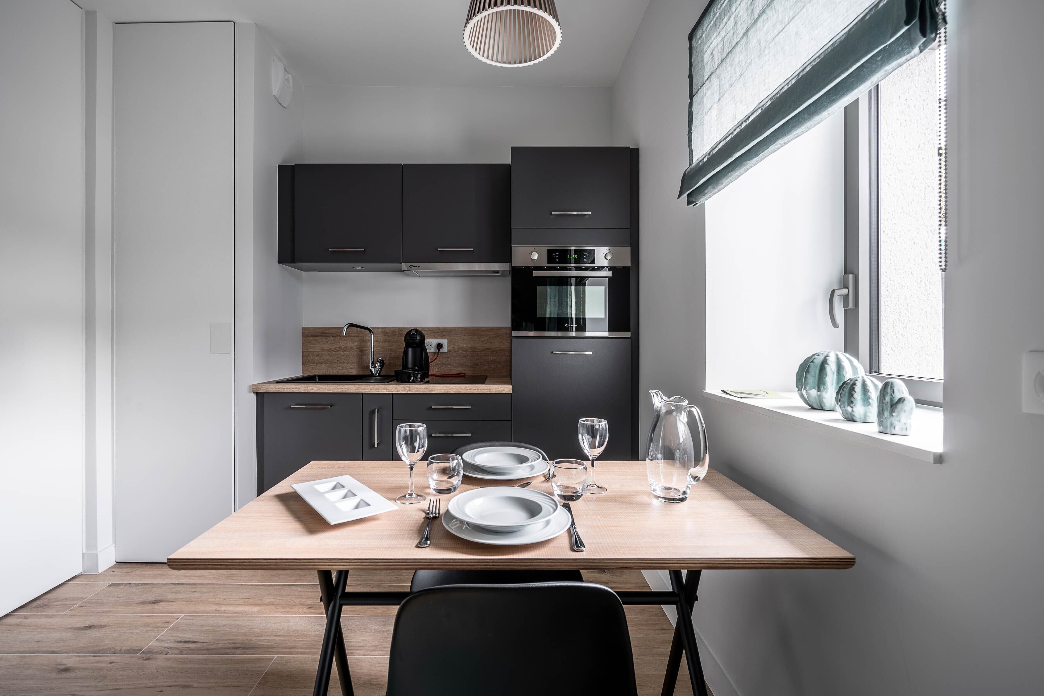 Una cocina moderna con armarios oscuros, una mesa de madera lista para comer y una ventana decorada.