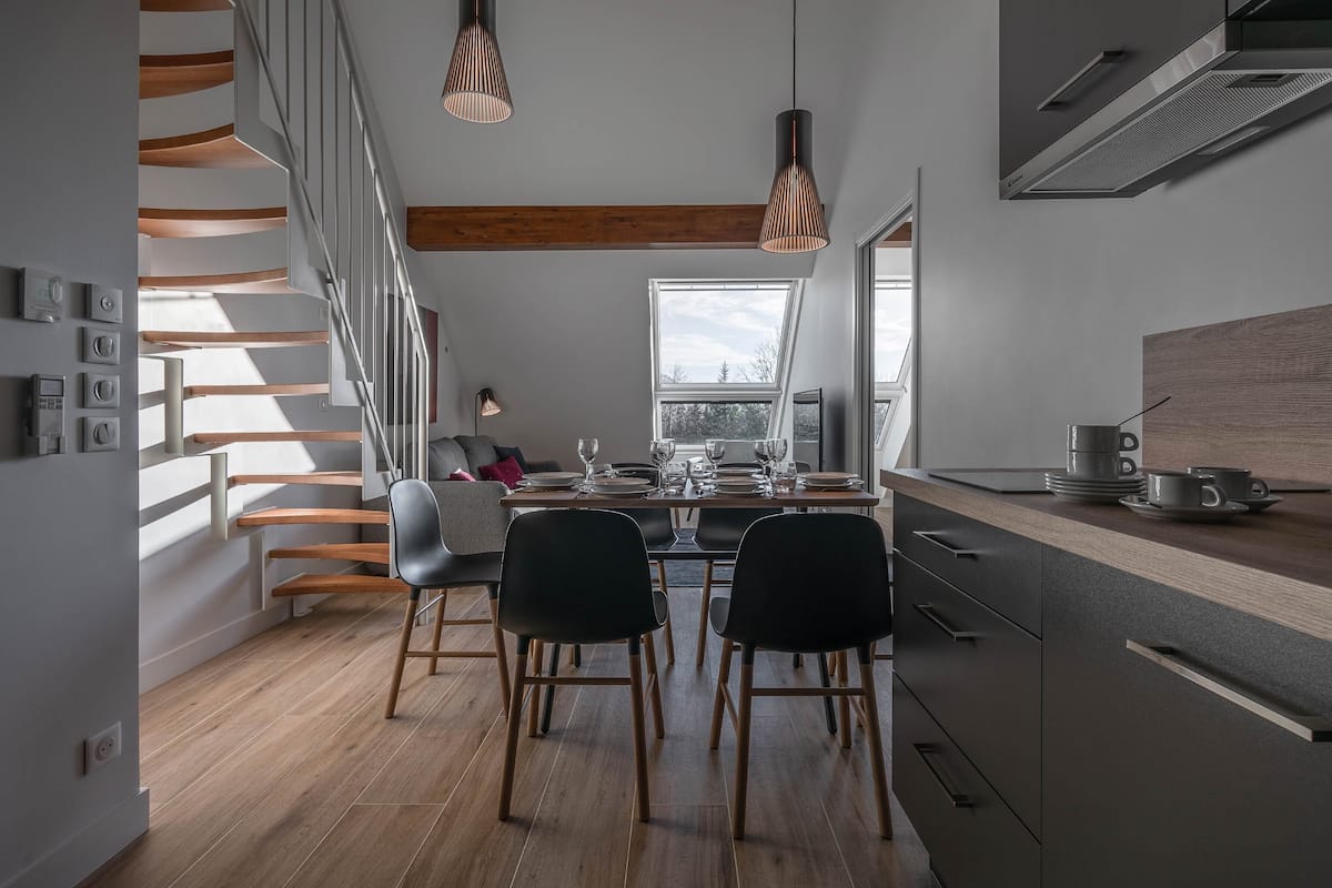 Une cuisine moderne avec un coin repas, un escalier en bois et de grandes fenêtres.