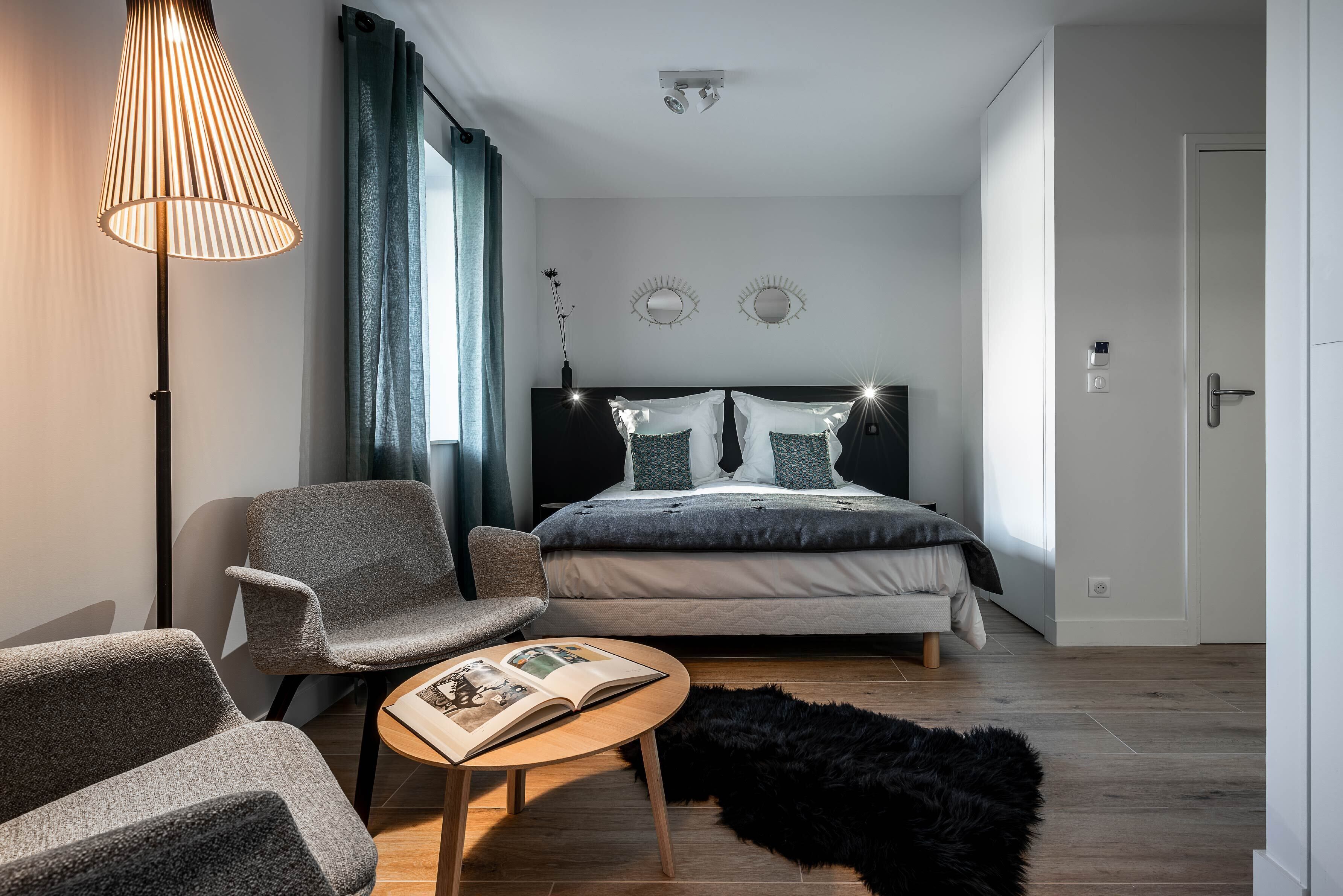 A modern bedroom with a bed, two chairs, a table, and a lamp.