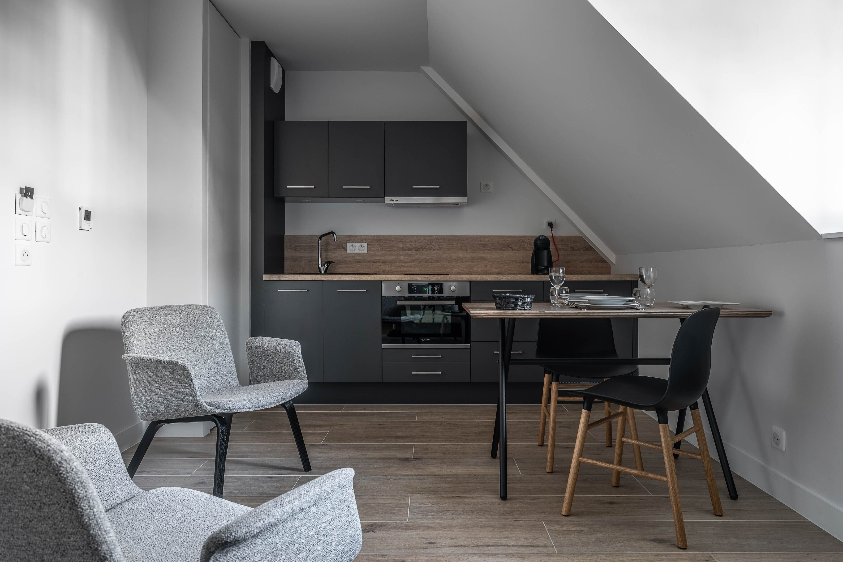 Una cocina moderna con armarios oscuros, encimera de madera y zona de comedor con dos sillas.