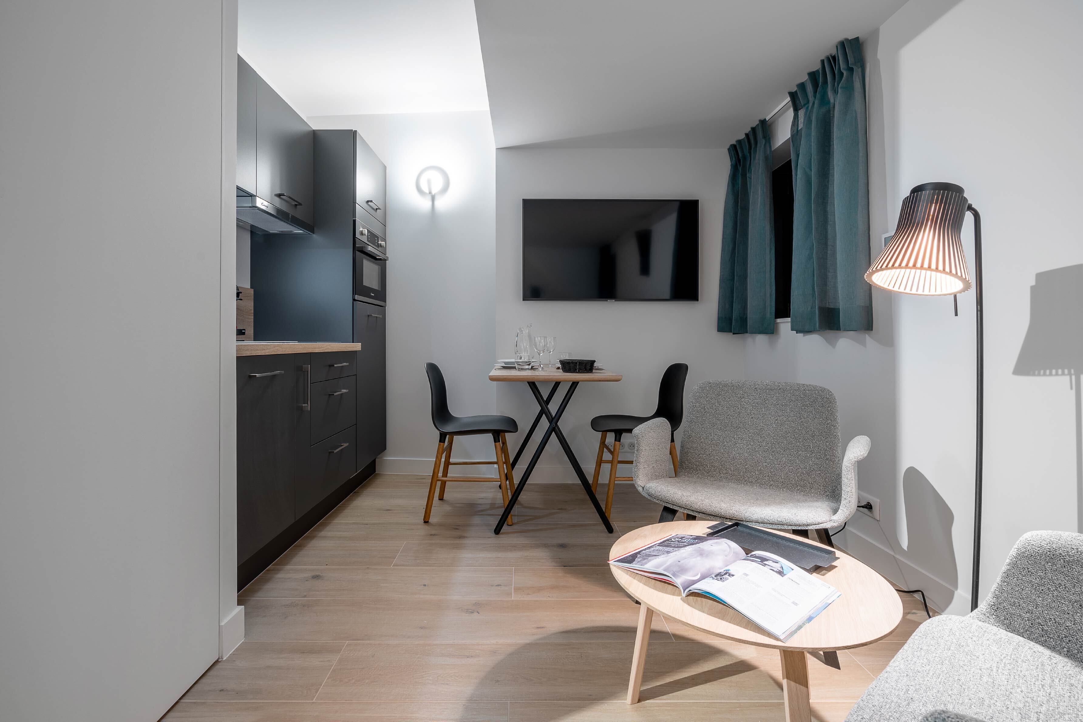 Una cucina moderna con mobili scuri, una zona pranzo con due sedie, un tavolo e un divano.