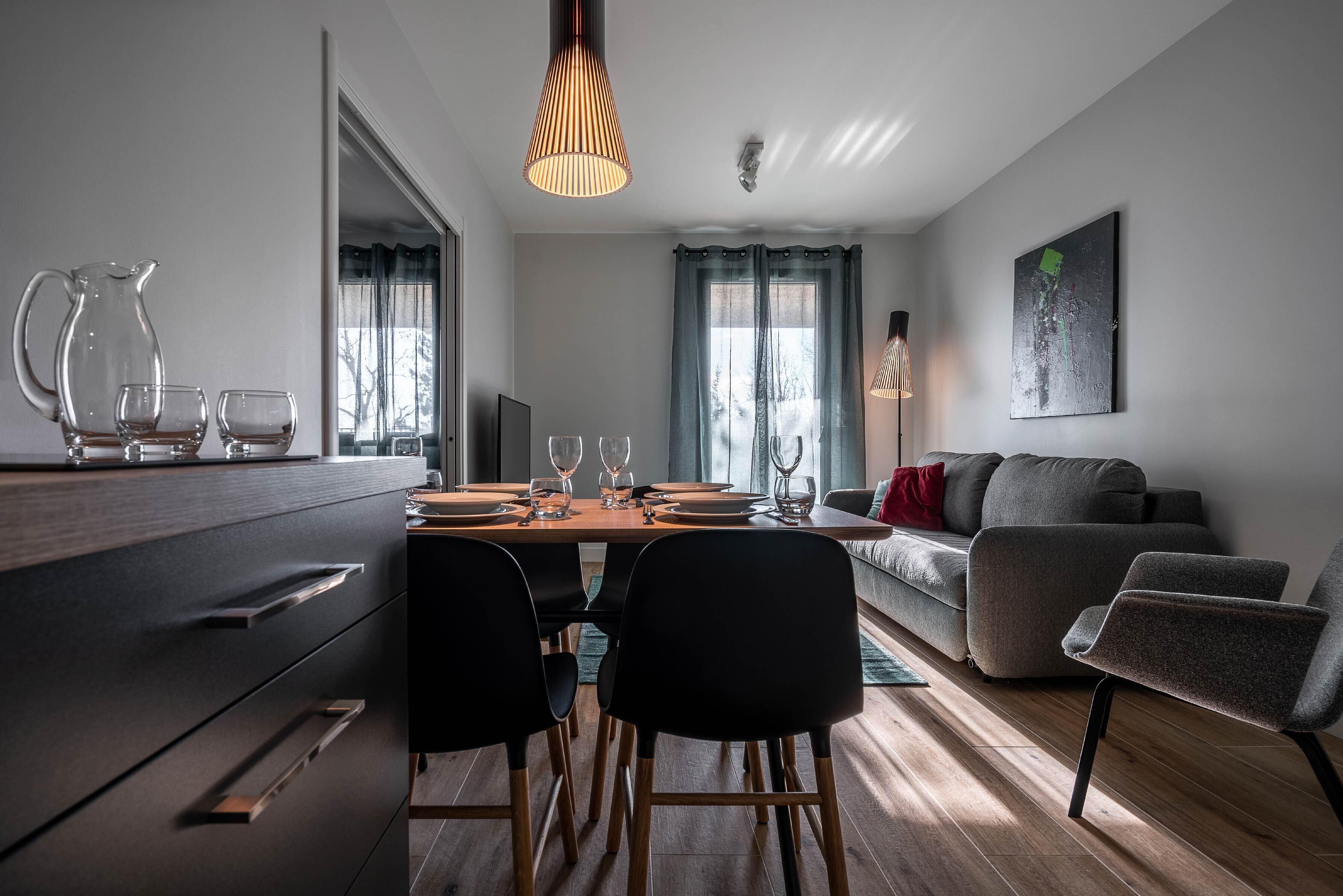 A modern living room with a dining area, a grey sofa, and a wooden floor.