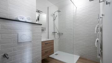 A modern bathroom with white brick walls, a glass shower enclosure, a wooden vanity, and a towel rack.