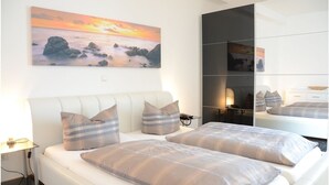 Un dormitorio moderno con una cama grande, una mesita de noche, una lámpara y un cuadro de una puesta de sol sobre rocas.