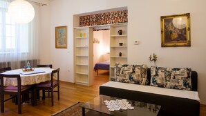 Een woonkamer met een bank, een eettafel met stoelen en een boekenkast.