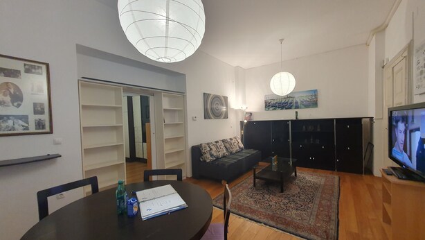 Een woonkamer met een ronde tafel, stoelen, een bank, een televisie en een grote lamp.