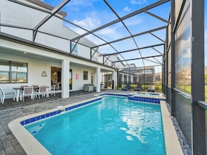A swimming pool with a glass enclosure, outdoor seating, and a patio area.