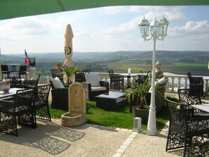 An outdoor seating area with tables and chairs, a statue, and a view of the landscape. - Les Balcons de l'Espérance (Limeuil)